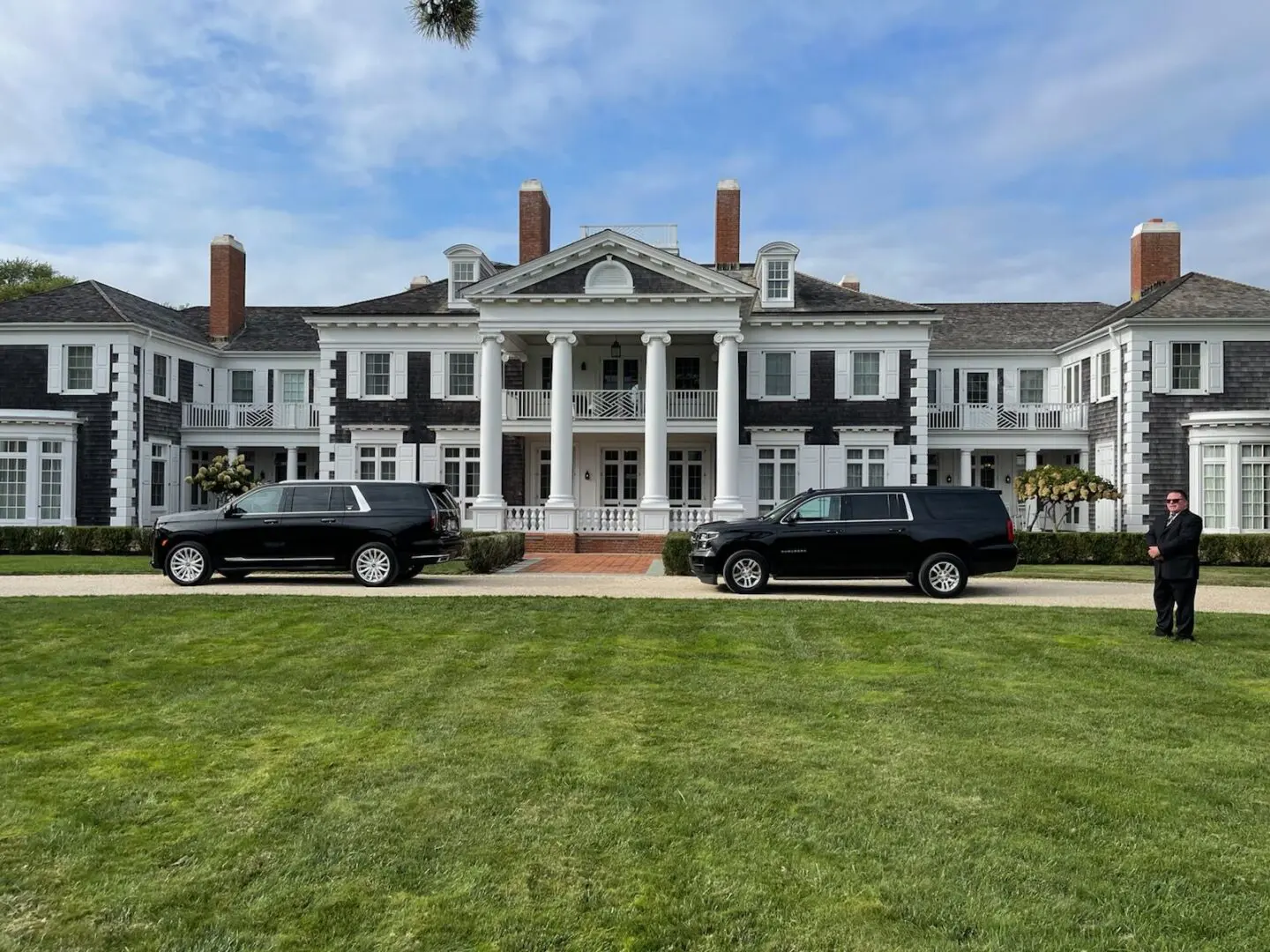Two black cars parked in front of a large white house.