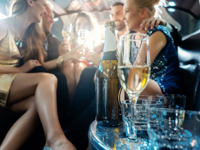 Women and men celebrating with drinks in a limousine car