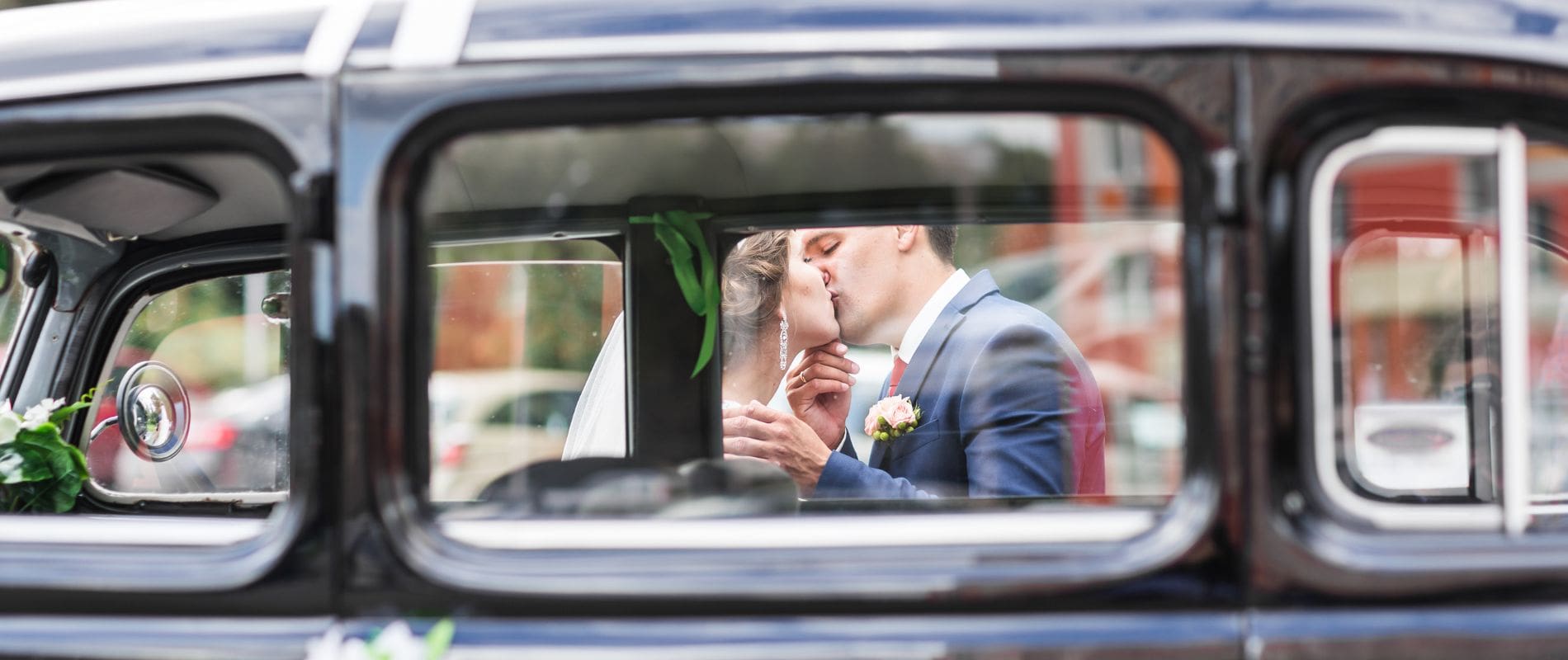 Wedding couple kissing in front of car